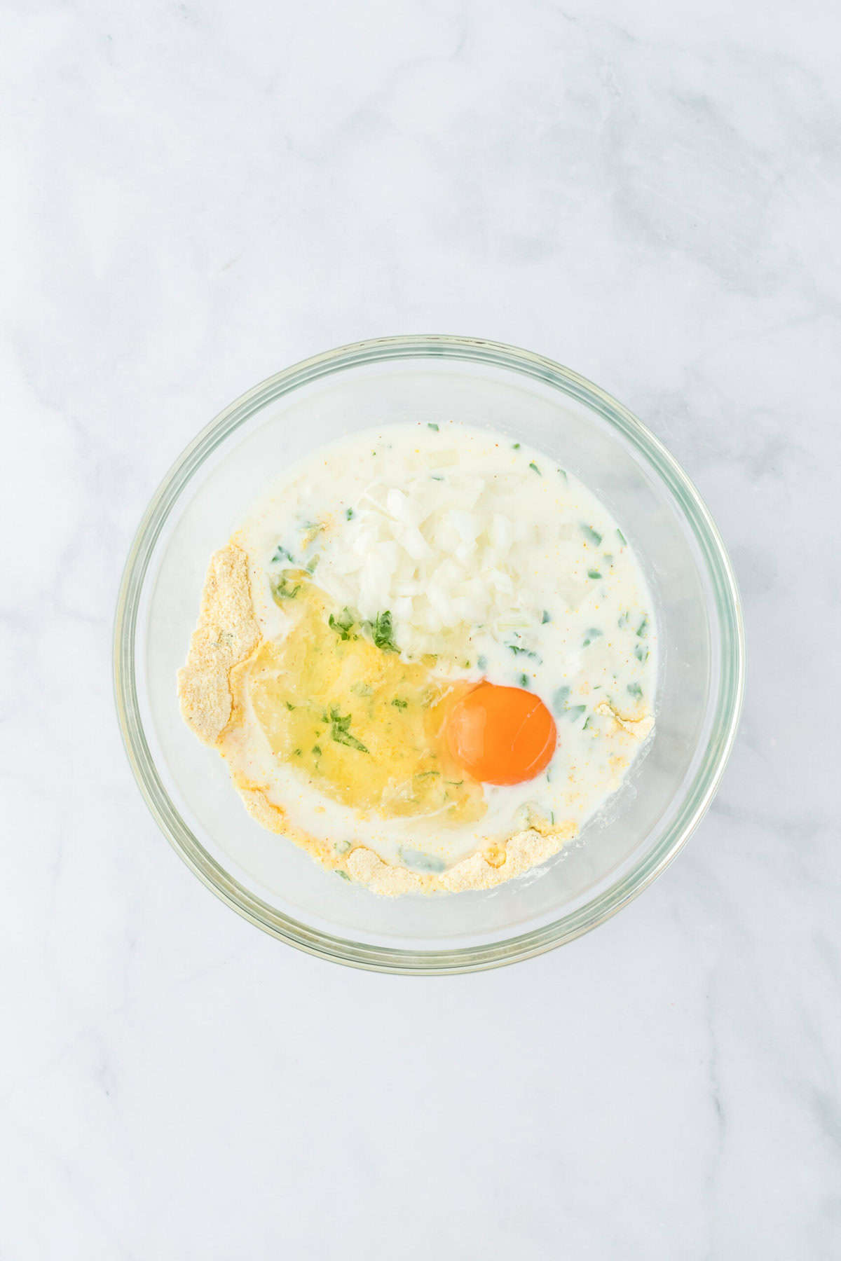 Egg, onion and milk added to hush puppy recipe ingredients in a clear bowl