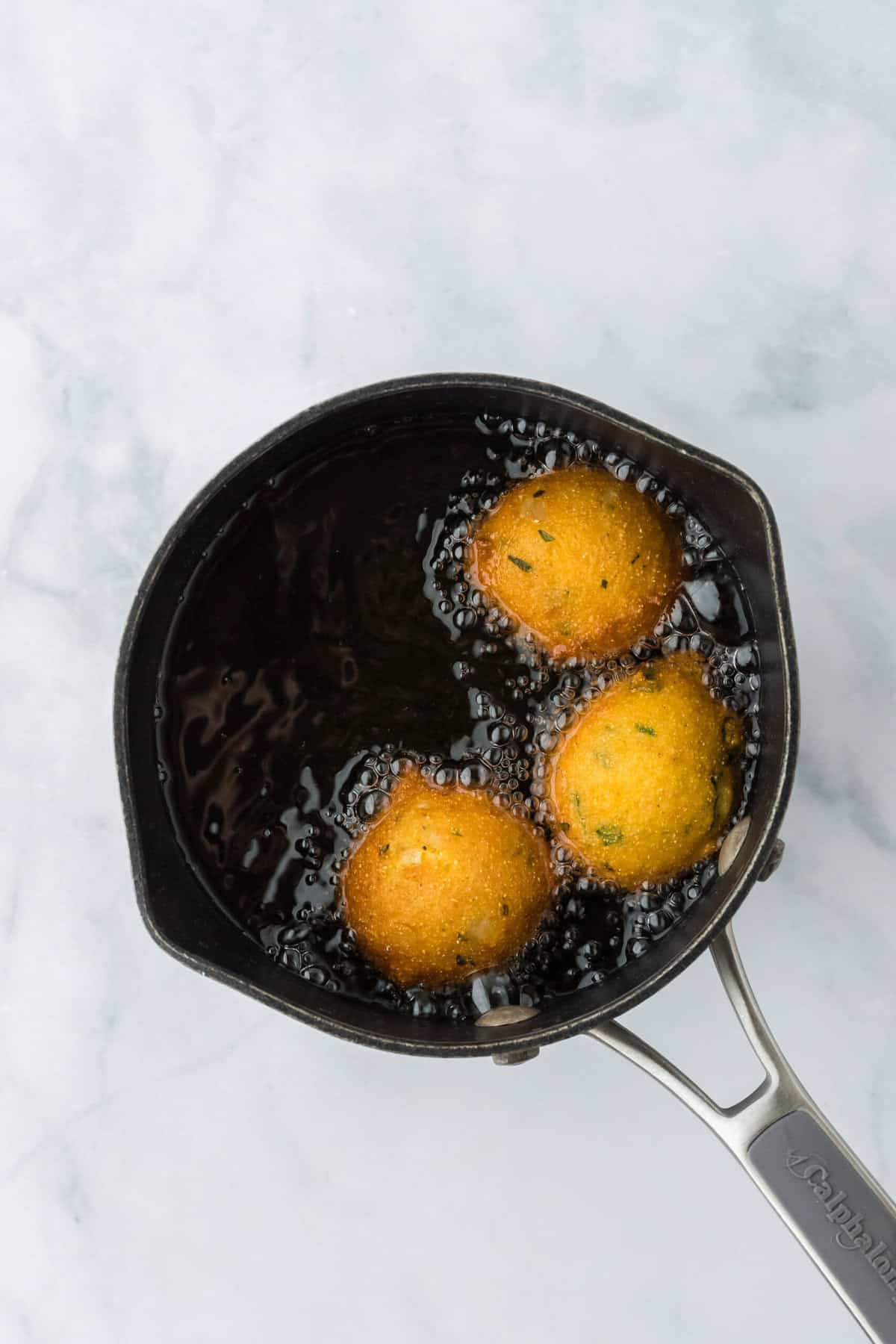 Hush puppies frying in a black skillet until golden on a white background