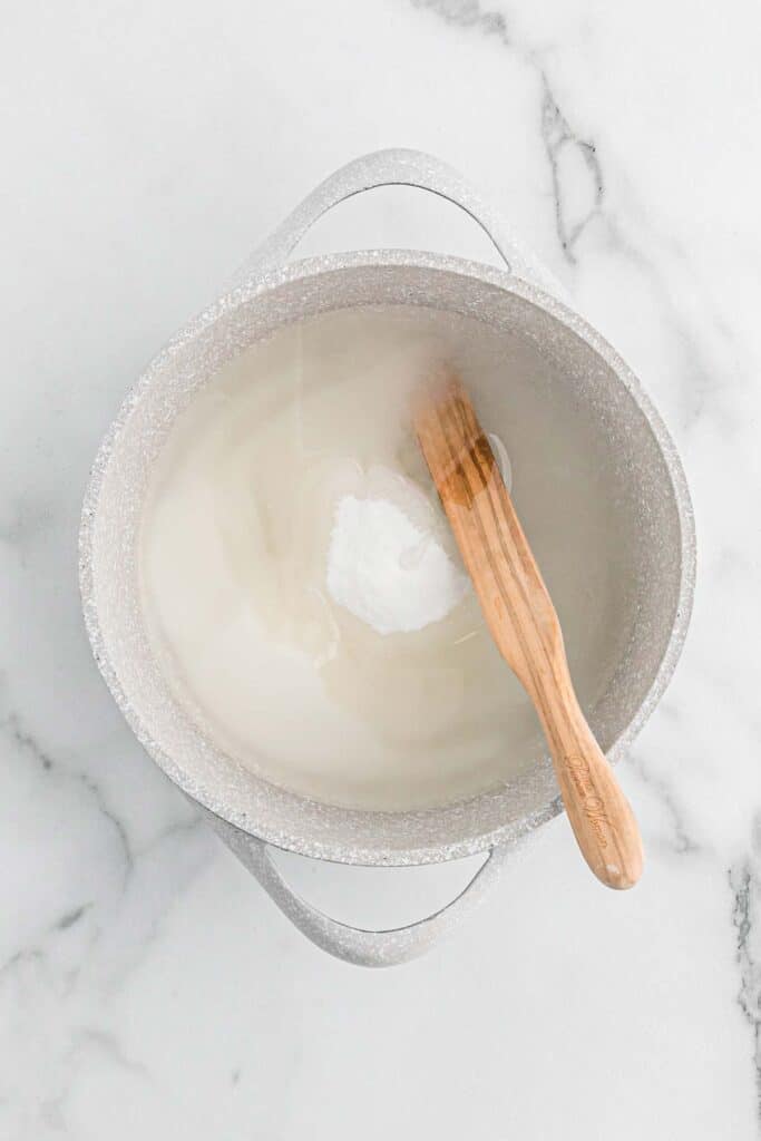 Sugar, corn syrup and water in a saucepan being stirred on white countertop