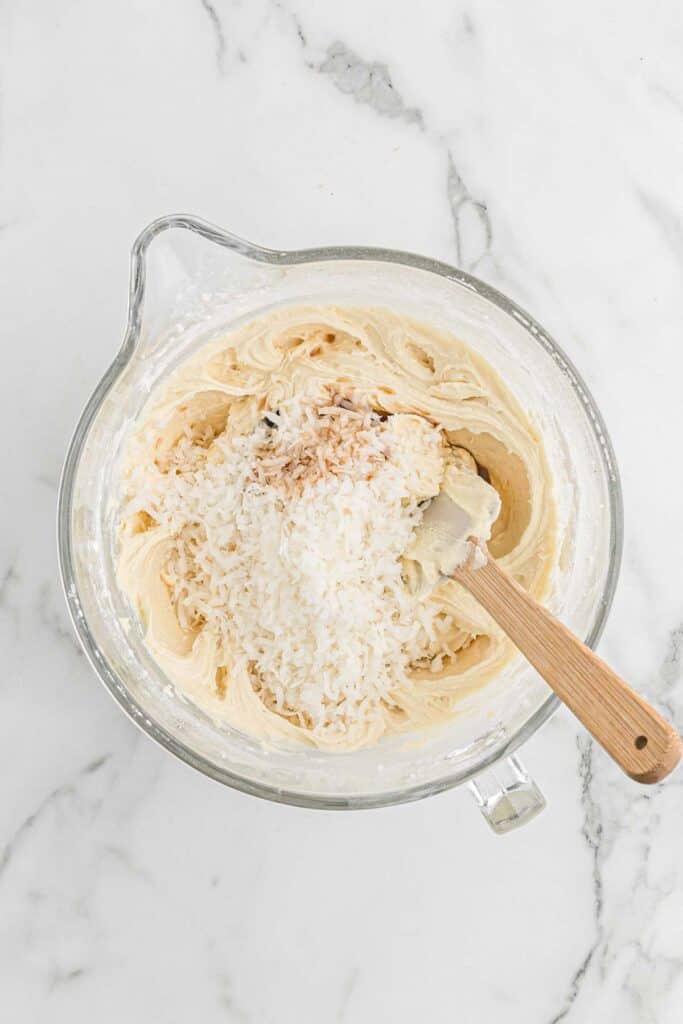 Shredded coconut flakes being added to cake batter on white countertop