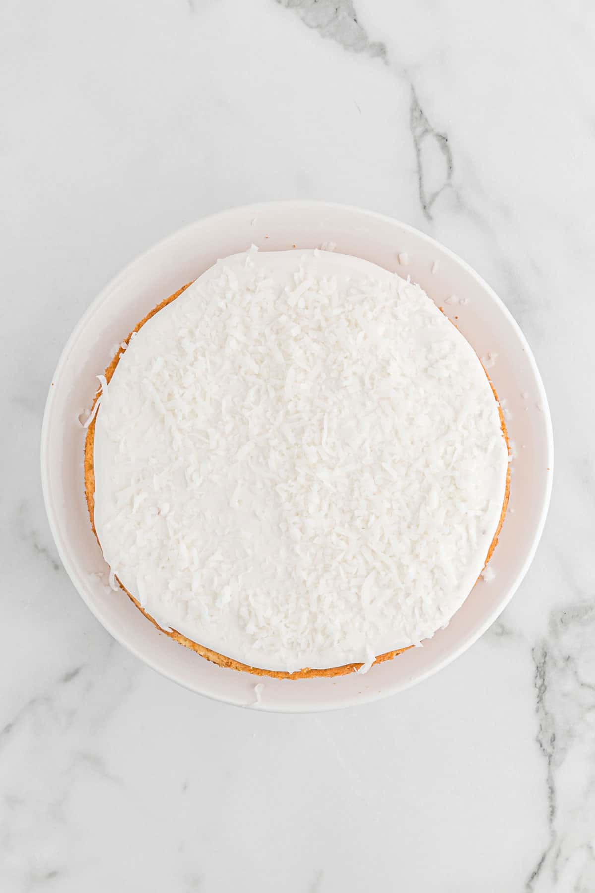 Overhead shot of coconut cake on a cake stand with frosting added in between layers.