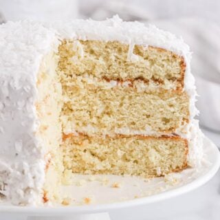 Easy coconut cake on a cake stand with pieces cut to show the inside layers.