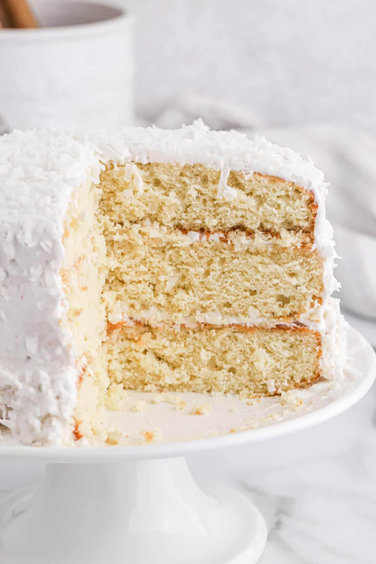 Easy coconut cake on a cake stand with pieces cut to show the inside layers.