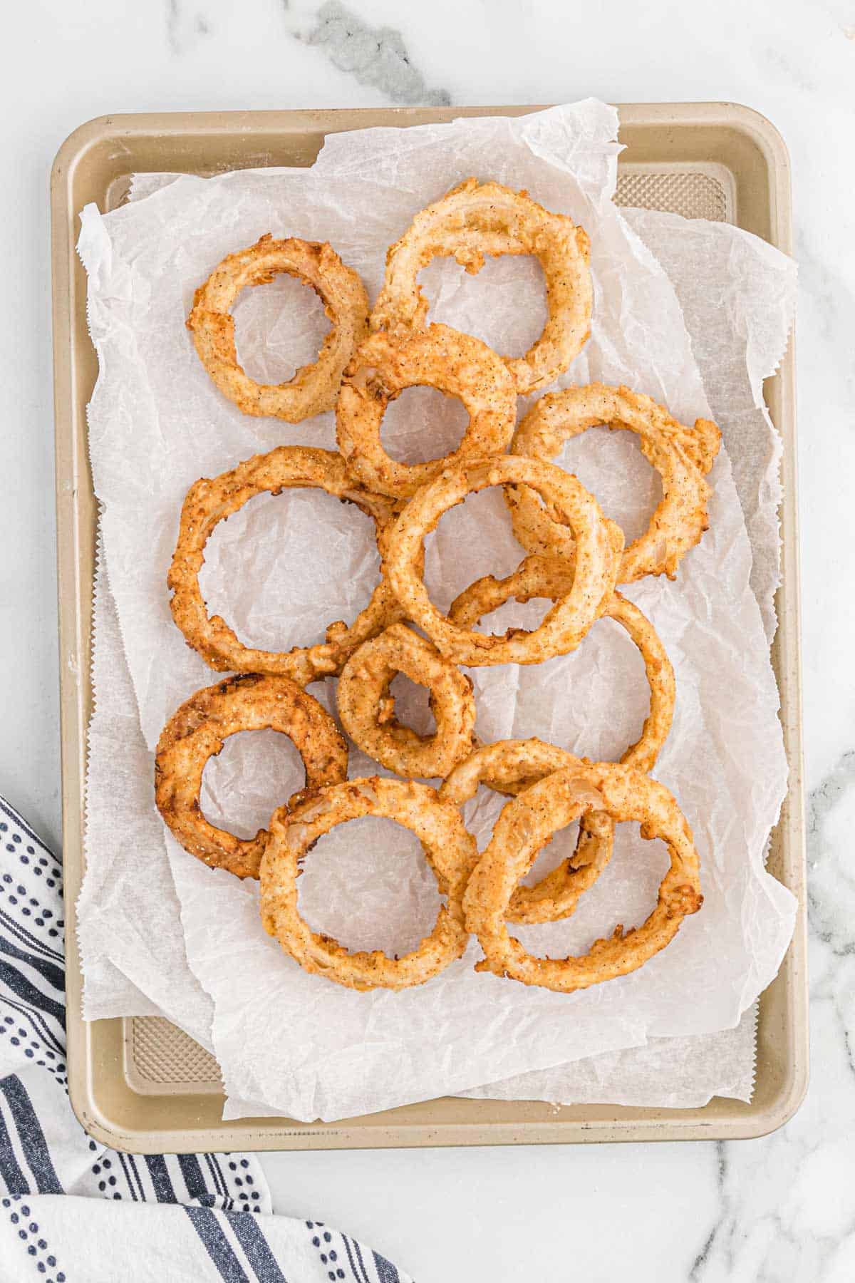 Fried onion rings on parchment and baking tray.