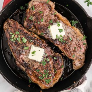 Cooked steaks in a pan topped with pats of butter.