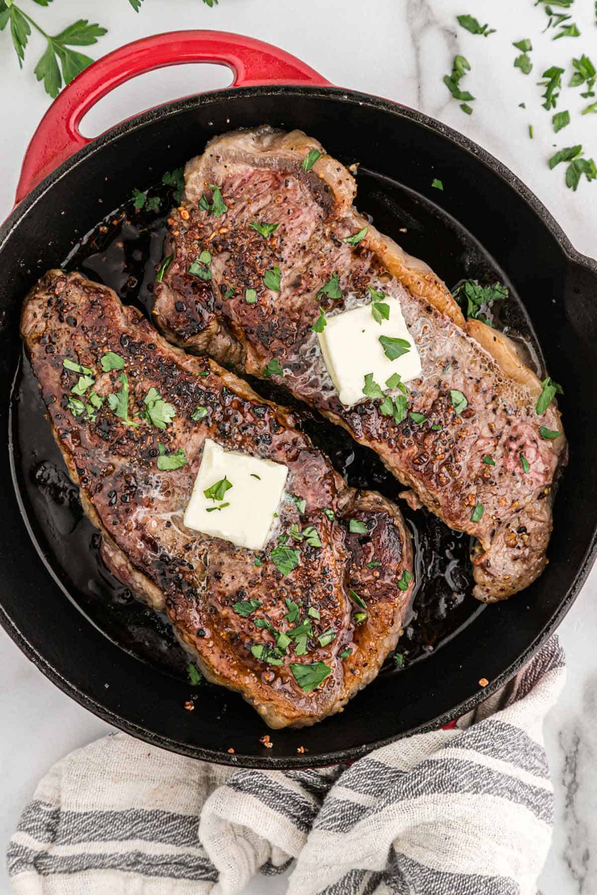 Cooked steaks in a pan topped with pats of butter.