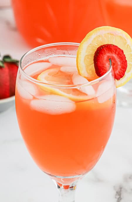 A glass of strawberry lemonade with a lemon slice and strawberry slice on the glass.