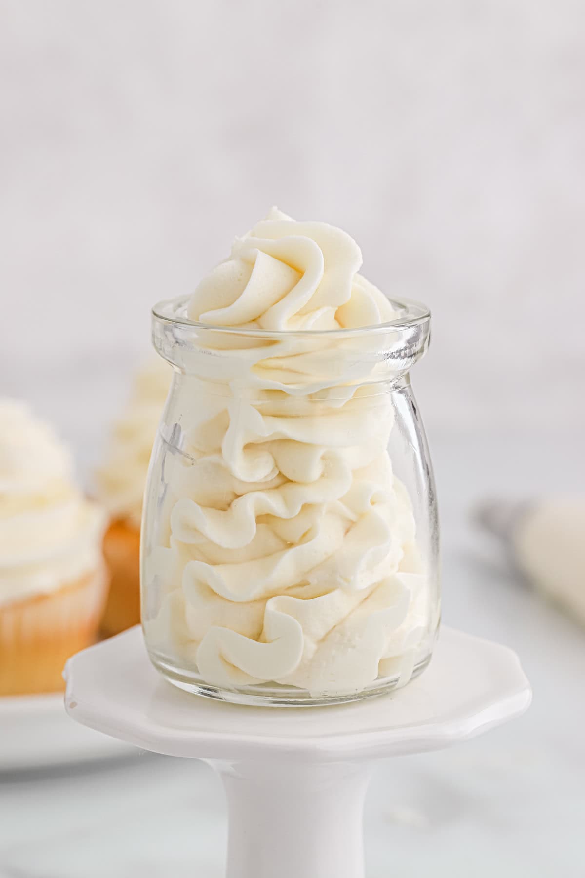 An American buttercream frosting in a glass piped high on a cupcake stand against a white background