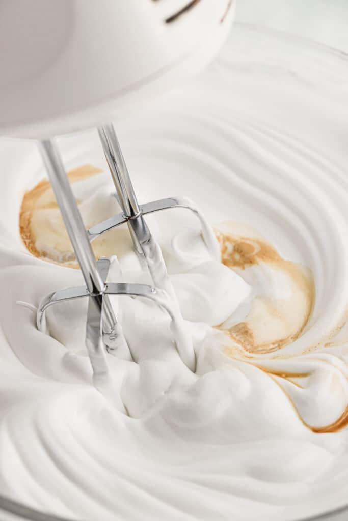 A hand mixer mixing the vanilla into the frosting.