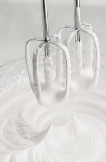 A hand mixer pulling the paddles out of the whipped frosting.