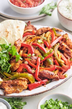 Sheet-pan chicken fajitas on a large white platter with tortillas ready to serve