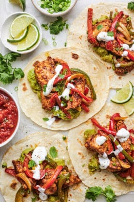Sheet-pan chicken fajitas served on tortillas with lemon wedges and sour cream