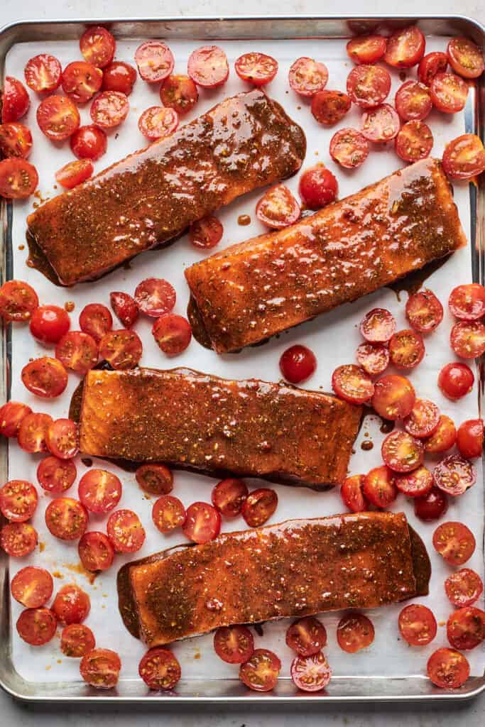 Jerk salmon filets on a sheet pan with cherry tomatoes before baking
