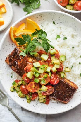 Jerk salmon being served on a bed of rice with cucumber salad