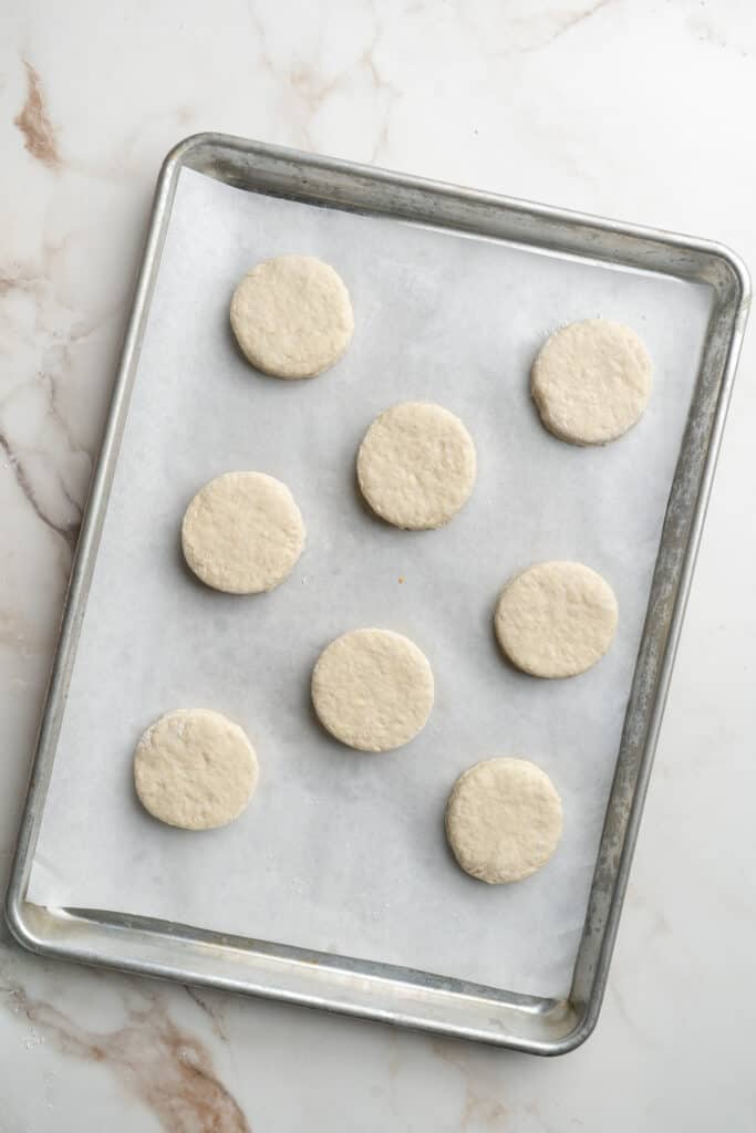 Biscuit rounds placed on a parchment lined baking sheet.