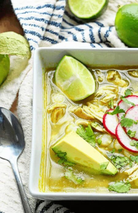 Mexican chicken pozole in a bowl with radishes, avocado, and lime on top.