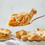 A slice of best apple pie with apple filling being lifted from pie plate ready to serve.