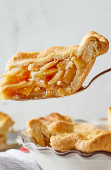 A slice of best apple pie with apple filling being lifted from pie plate ready to serve.