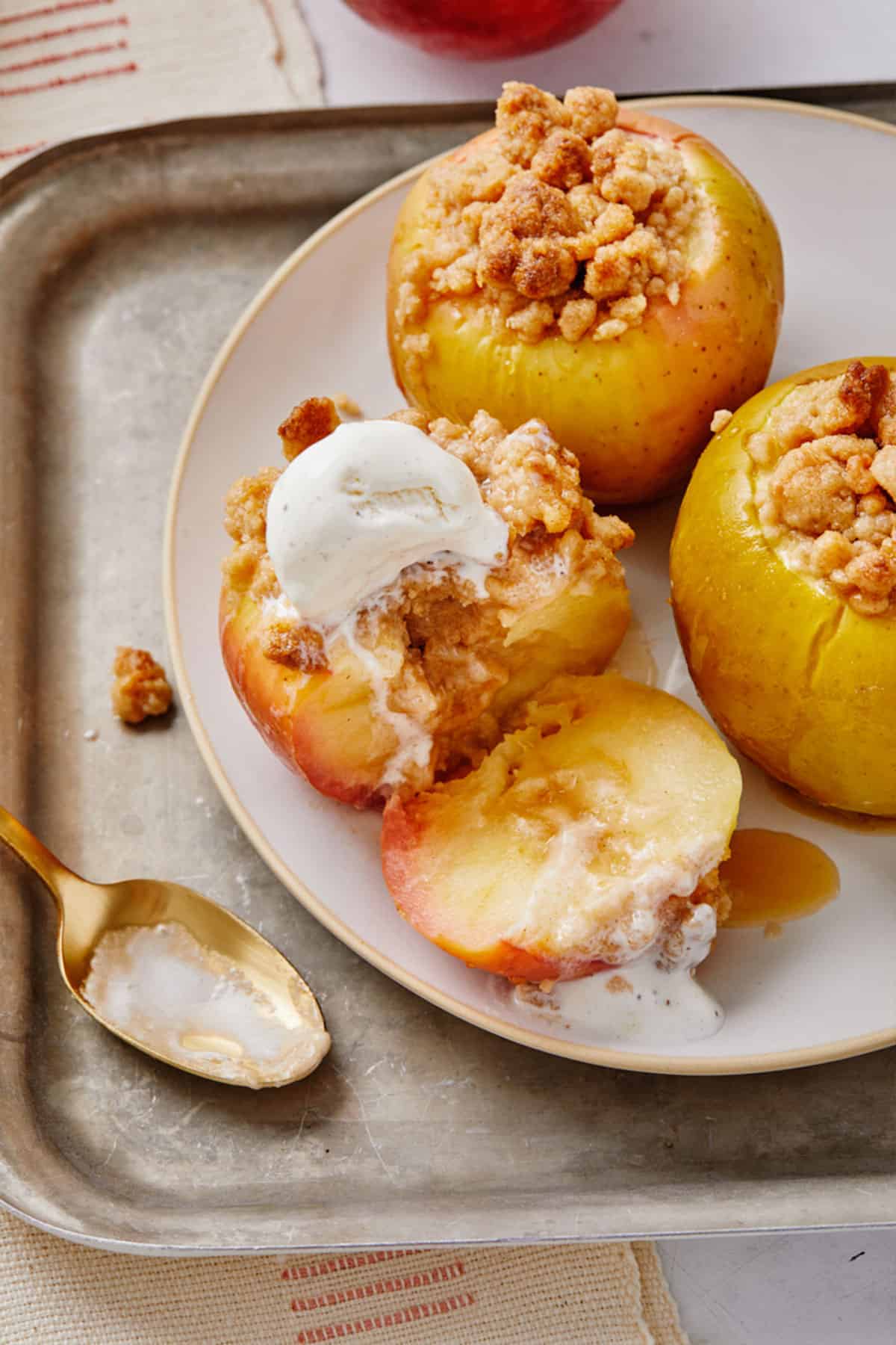 Three baked apples on a plate and one is topped with ice cream and cut into so you can see the inside.
