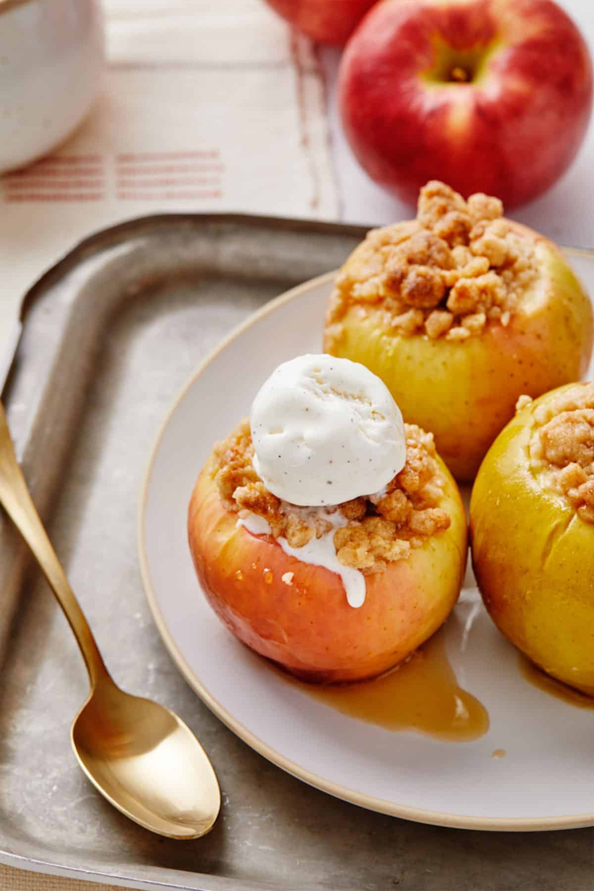 Baked apples with crumble topping on a plate and one topped with a scoop of ice cream.