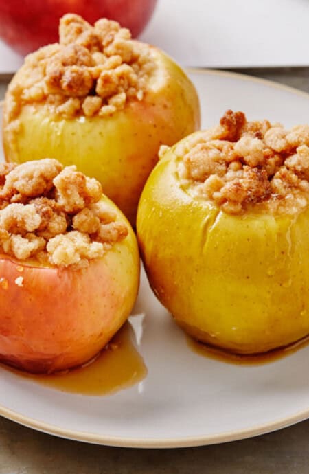 Baked apples with crumb topping on a plate with cinnamon sticks.