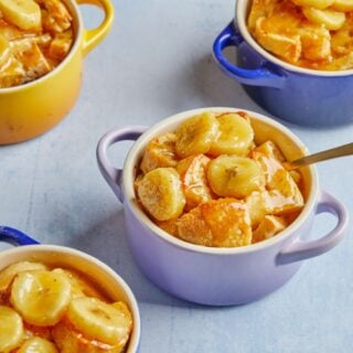 Blue ramekins of bananas foster bread pudding on the table with a spoon dipping into the one in front.