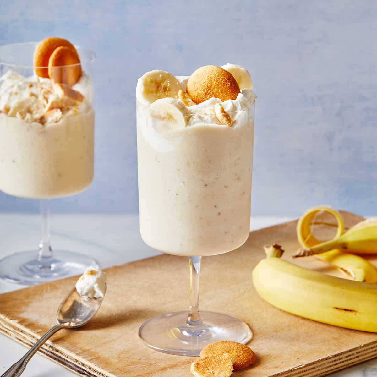 Two homemade banana milkshakes in glasses with whipped cream, bananas and nilla wafer on top.