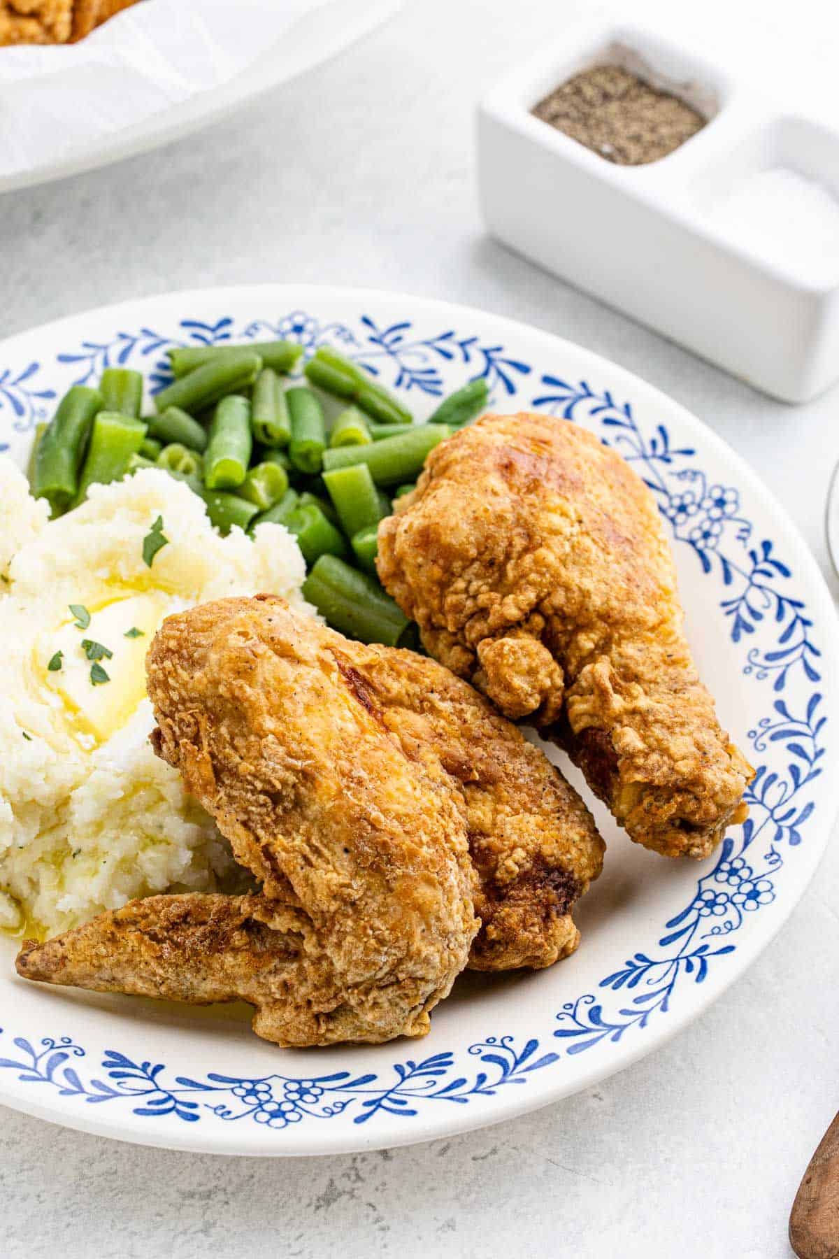 A plate of fried chicken with potatoes and green beans.