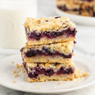 A stack of blueberry crumble bars on a plate with more in the background.