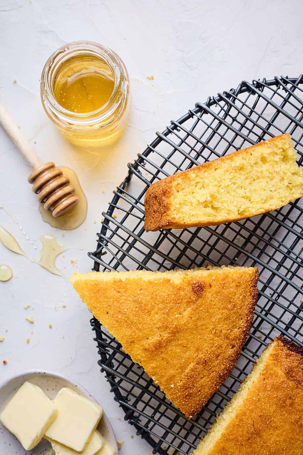 Delicious honey cornbread slice sitting on a cooling rack with honey next to it.