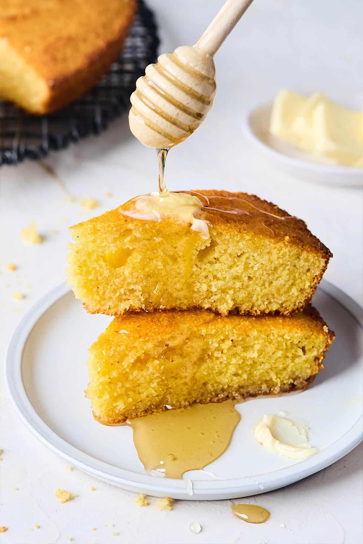 Slices of cornbread with honey and butter on top and honey being drizzled over the top.