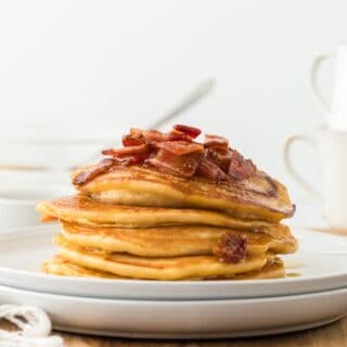 Brown sugar pancakes stacked up on a white plate and topped with maple bacon syrup.
