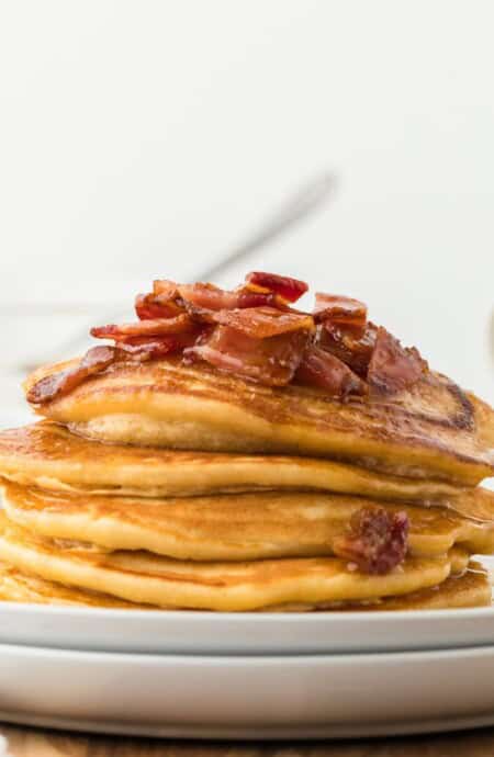 Brown sugar pancakes stacked up on a white plate and topped with maple bacon syrup.