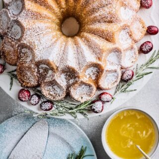 A buttered rum eggnog cake on a white plate dusted with powdered sugar and a bowl of sauce on the side.