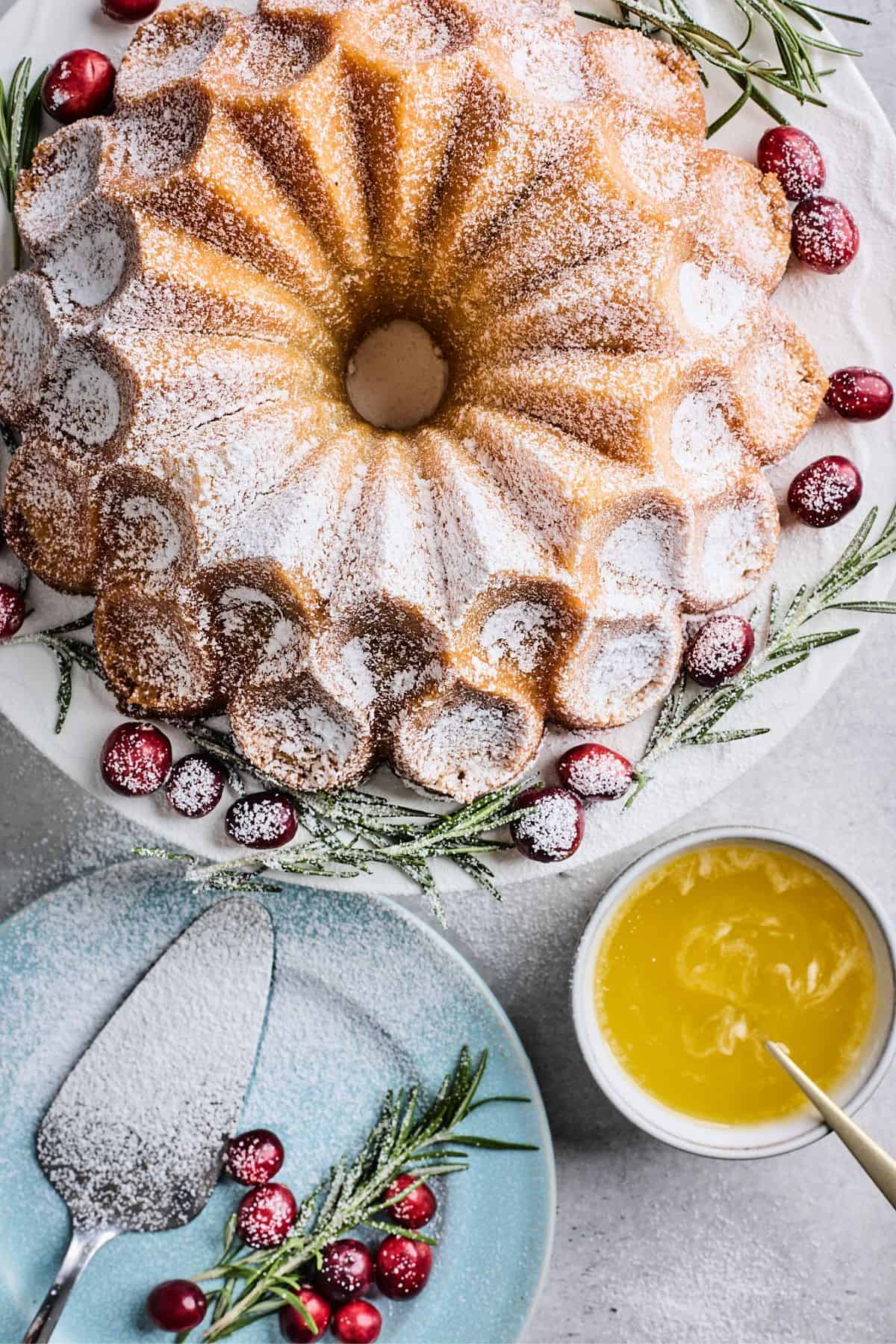 A buttered rum eggnog cake on a white plate dusted with powdered sugar and a bowl of sauce on the side.