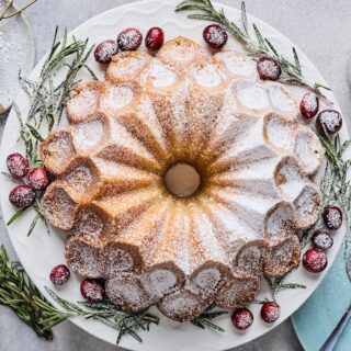 A buttered rum eggnog cake on a plate garnished with cranberries and rosemary.
