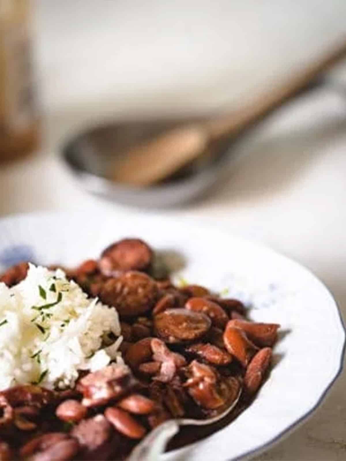 Red beans in a bowl topped with white rice and a spoon in the bowl.