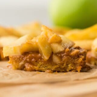 Caramel apple bars on a piece of parchment on the table showing the chewy base and apple topping.