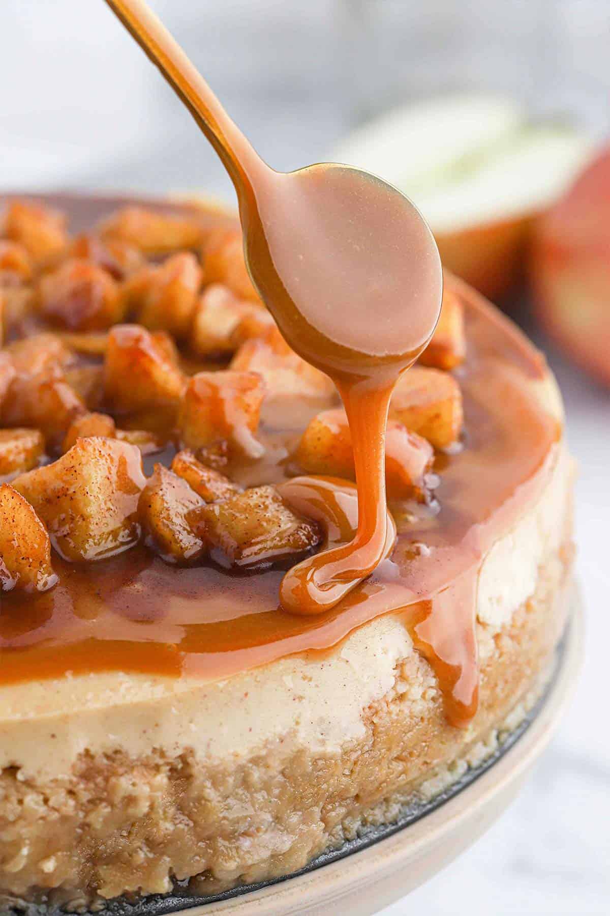 A spoon drizzling caramel sauce over the top of apple caramel cheesecake.