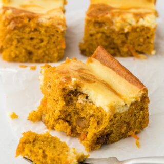 Three mango carrot cake swirl bars sitting on a square, white plate on top of a colorful cloth.