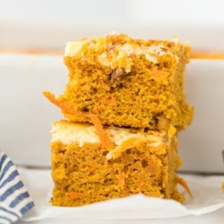 Two carrot cake bars stacked on top of one another on a white plate.