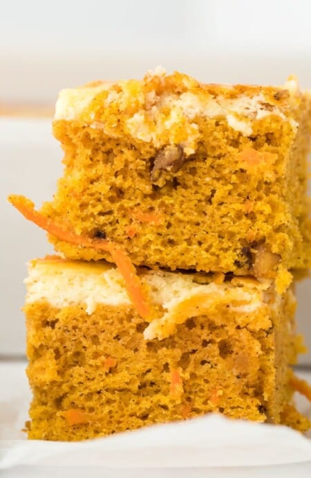 Two carrot cake bars stacked on top of one another on a white plate.