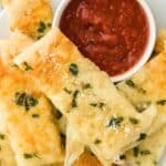 Garlic Cheese Breadsticks on a white plate with pizza sauce in a bowl