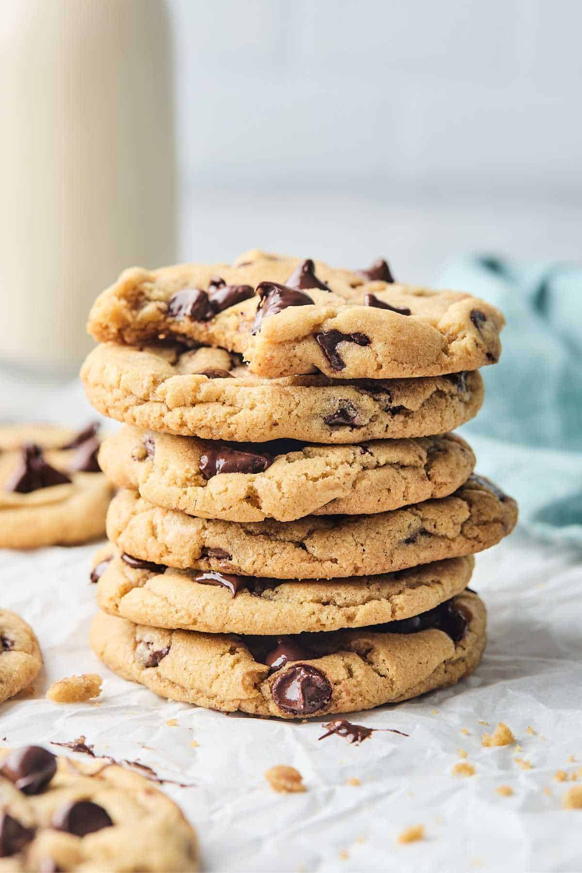 A stack of chewy chocolate chip cookies against white background with pitcher of milk
