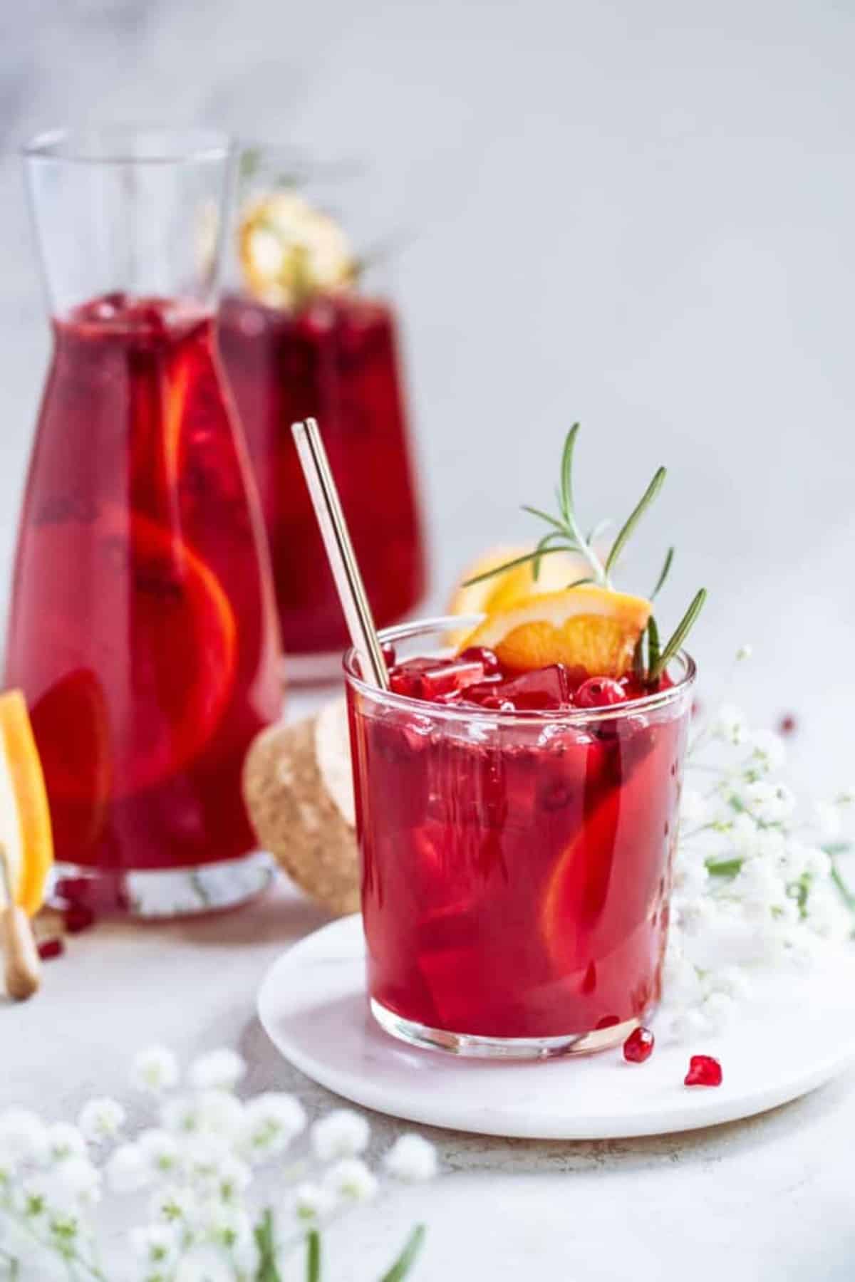A close up of a short glass and carafe of pomegranate punch for the holidays