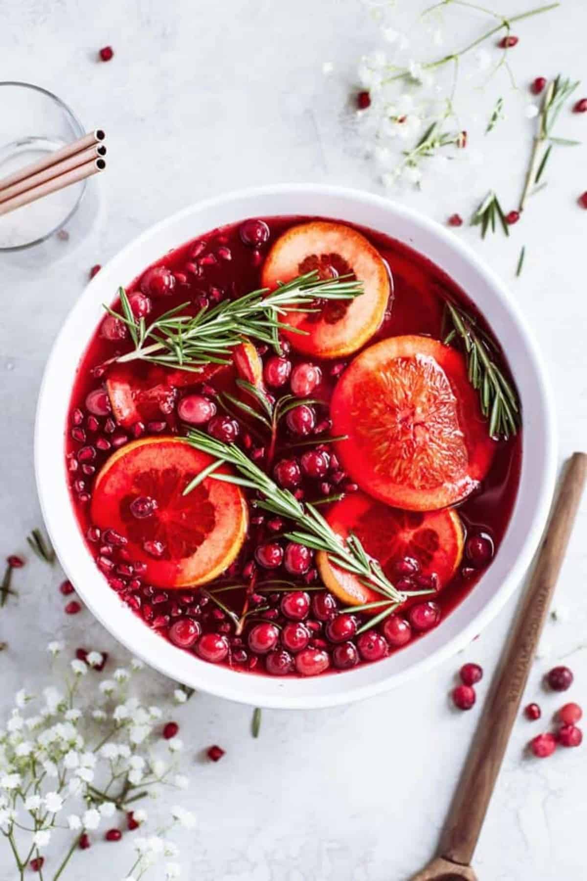 An overhead of a white punch bowl filled with Christmas punch and garnished with cranberries, pomegranate seeds, orange slices and rosemary