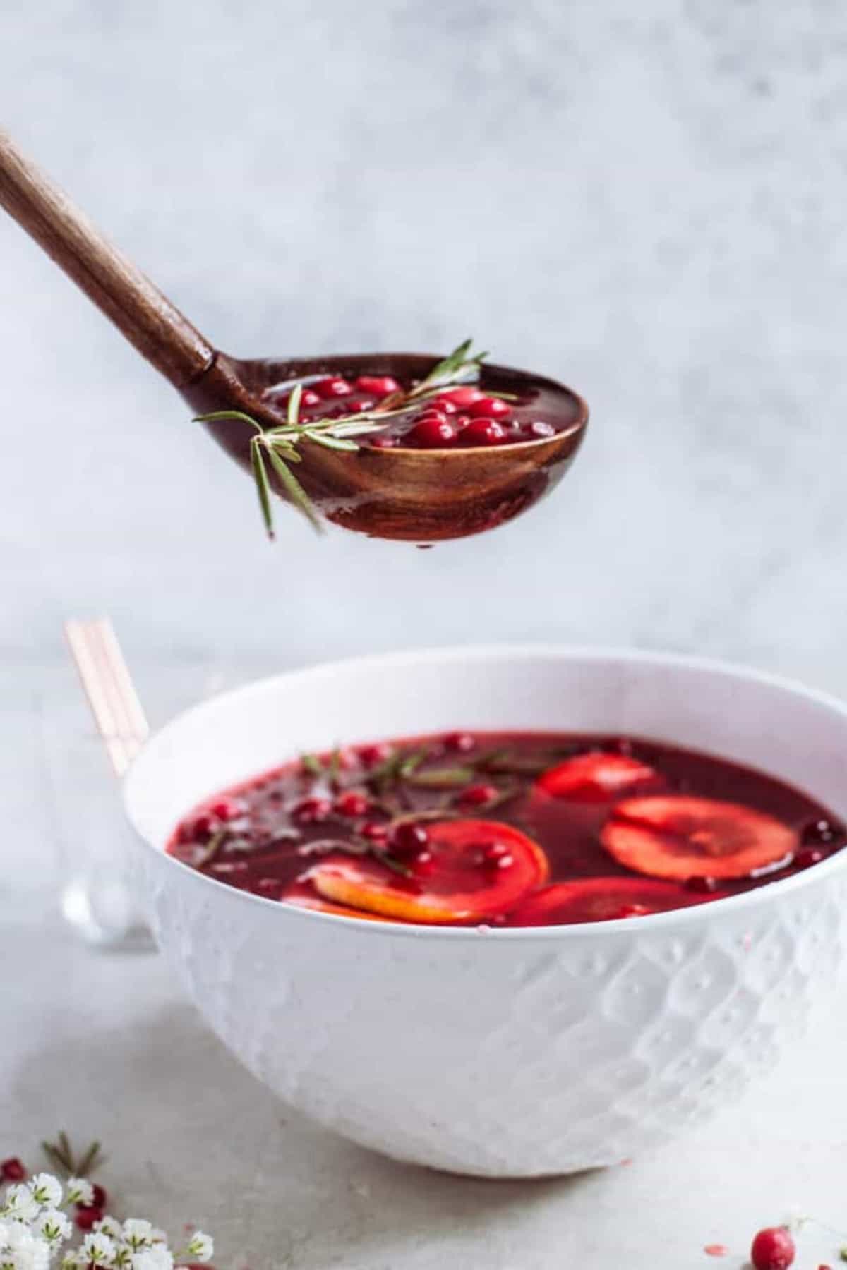 A large white punch bowl filled with Christmas punch with a large spoon about to serve some