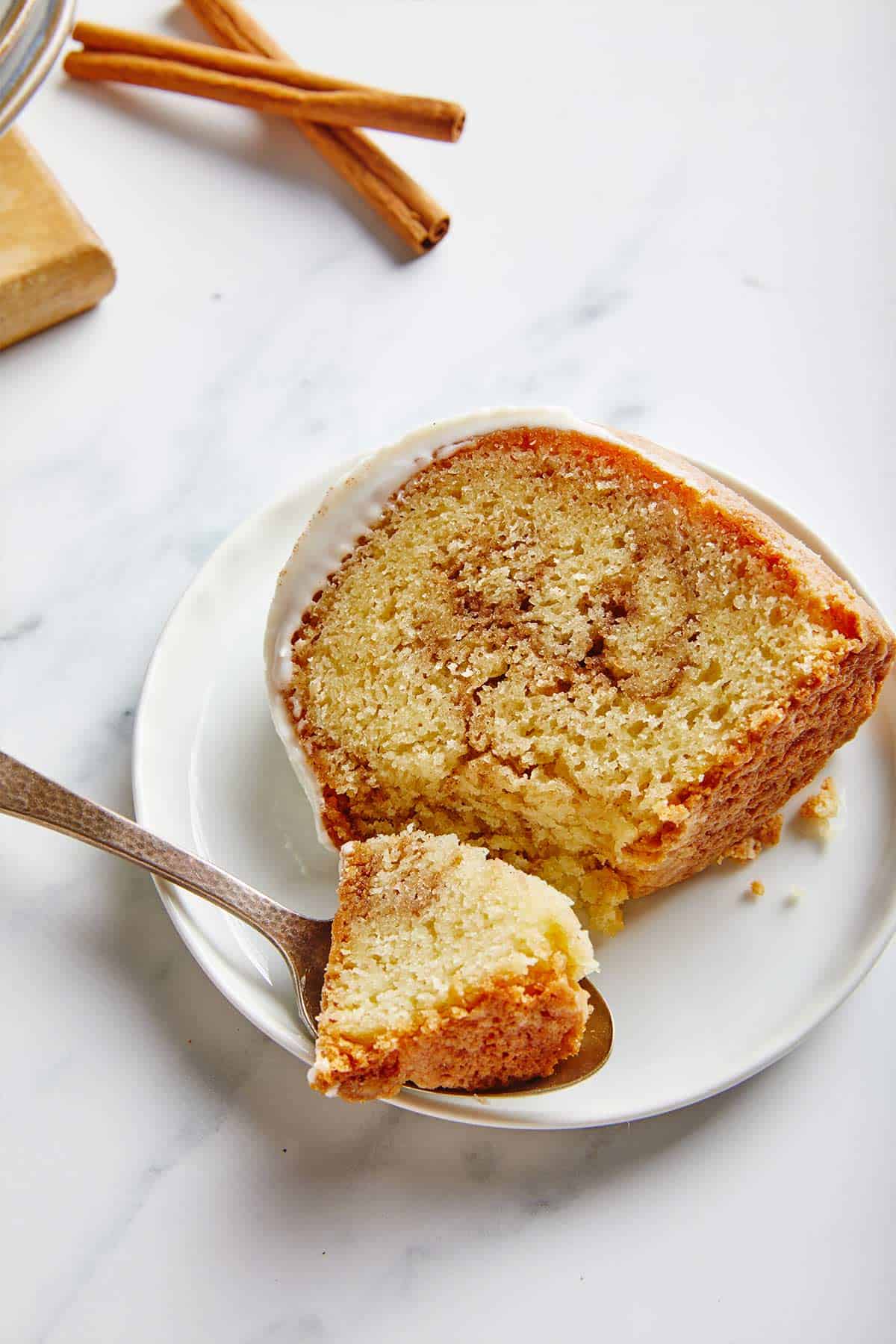A piece of cinnamon pound cake on a plate with a bite on a spoon.