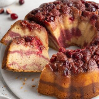 A cranberry bundt cake on a platter with a couple slices cut and laying over on the side.