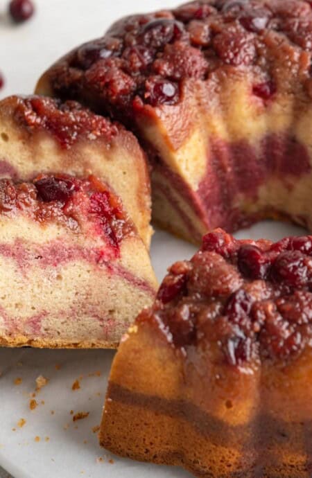 A cranberry bundt cake on a platter with a couple slices cut and laying over on the side.